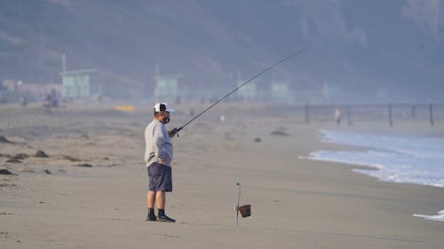 Free Man Standing on Beach Sand Holding a Fishing Rod Stock Photo