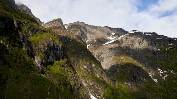 Scenic view of rocky mountains with patches of snow and lush greenery in daylight.