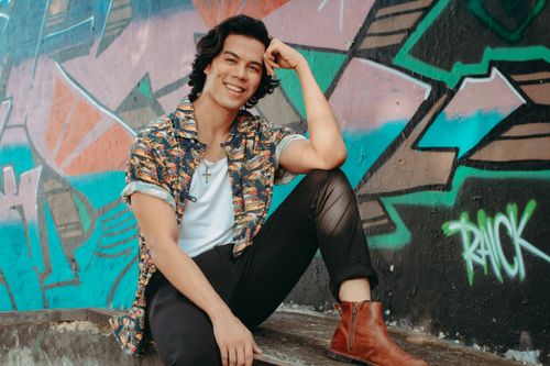 Free Smiling man with stylish attire posing against a vibrant graffiti wall outdoors. Stock Photo