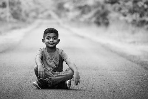 Grayscale Photo of Boy Sitting on the Floor