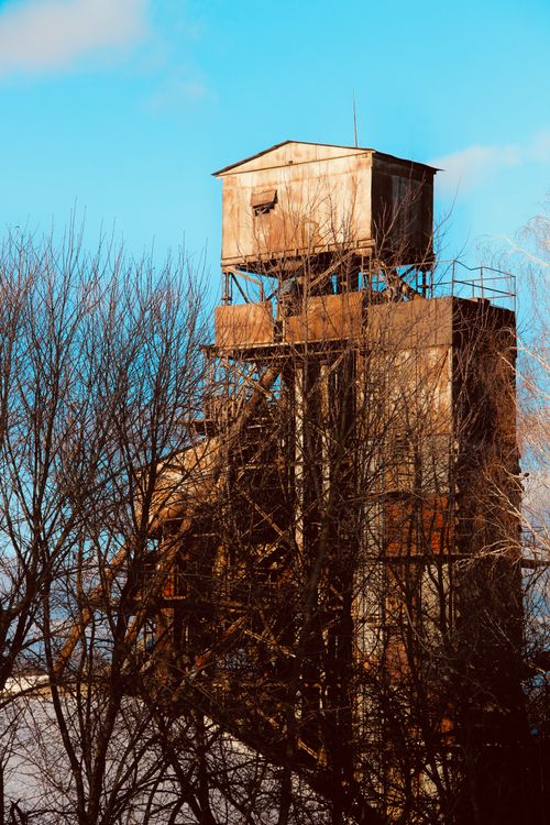 Free An old, rustic industrial structure surrounded by bare trees under a clear blue sky. Stock Photo