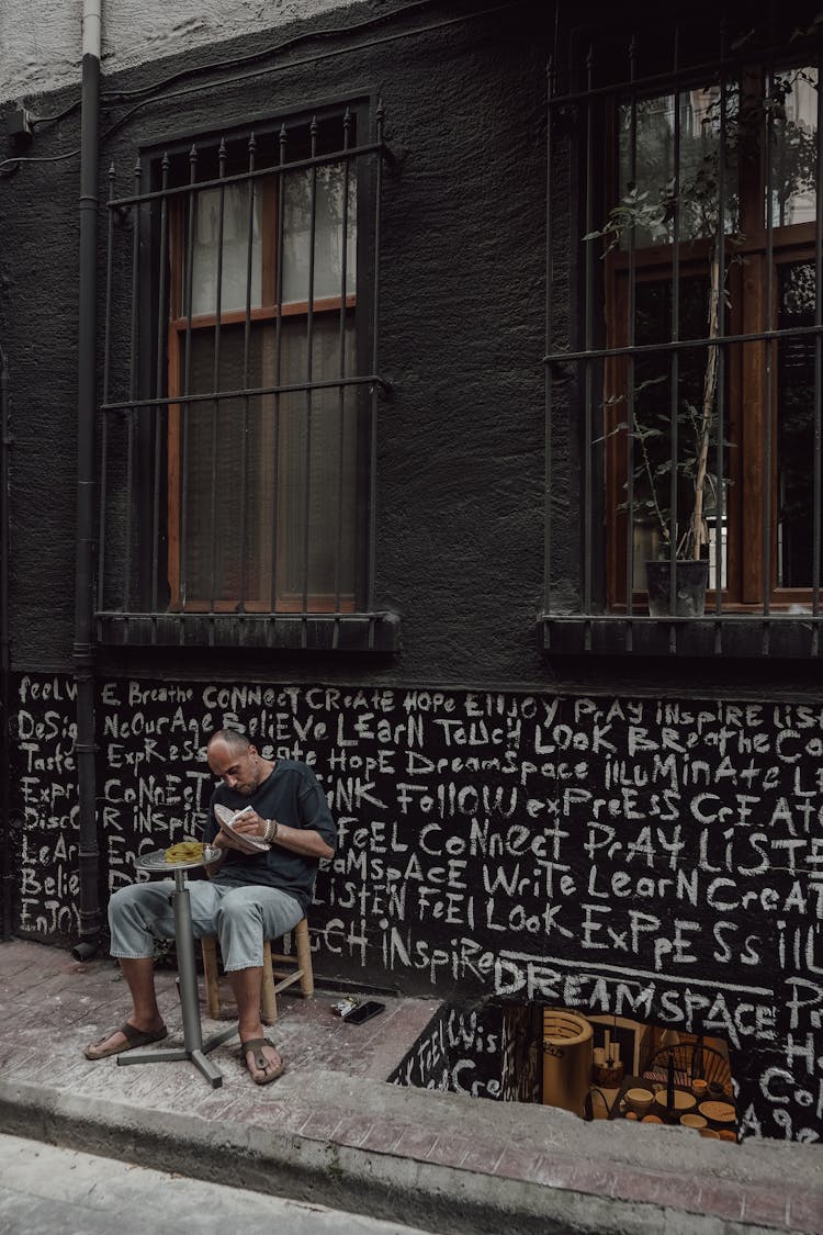 Man Sitting At Table Near Black City Wall With Art