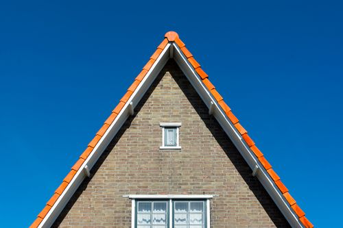 Free Symmetrical brick house gable with triangular shape and red roof tiles against a clear blue sky. Stock Photo