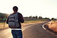 日落时分，旅行者背着背包，走在乡村蜿蜒的道路上，这象征着冒险和自由