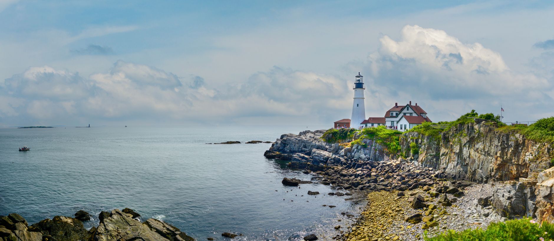 Panoramic view of Portland Head Light on Maine's rugged coastline under a clear sky.
