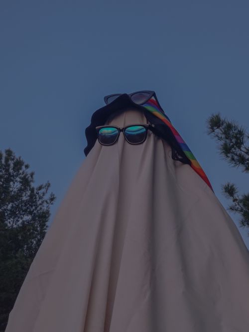 Free A ghost costume with sunglasses and a rainbow hat, set against a twilight outdoor background. Stock Photo