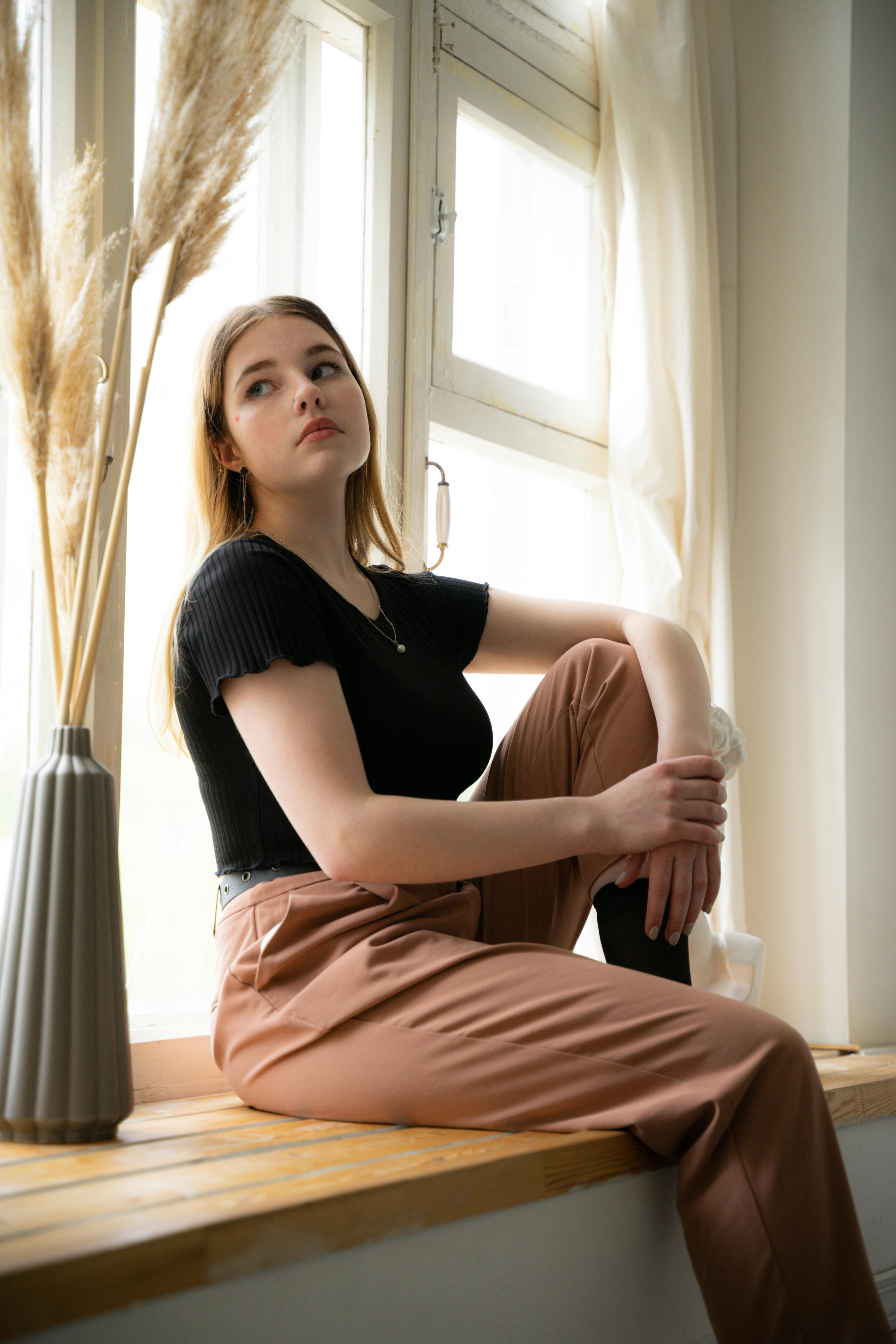 Woman in Black Shirt Brown Pants Sitting on Window Sill  Free Stock Photo