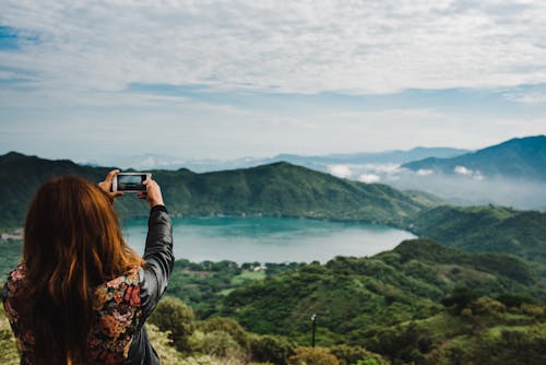 Woman Taking Photo of Green-covered Mountain