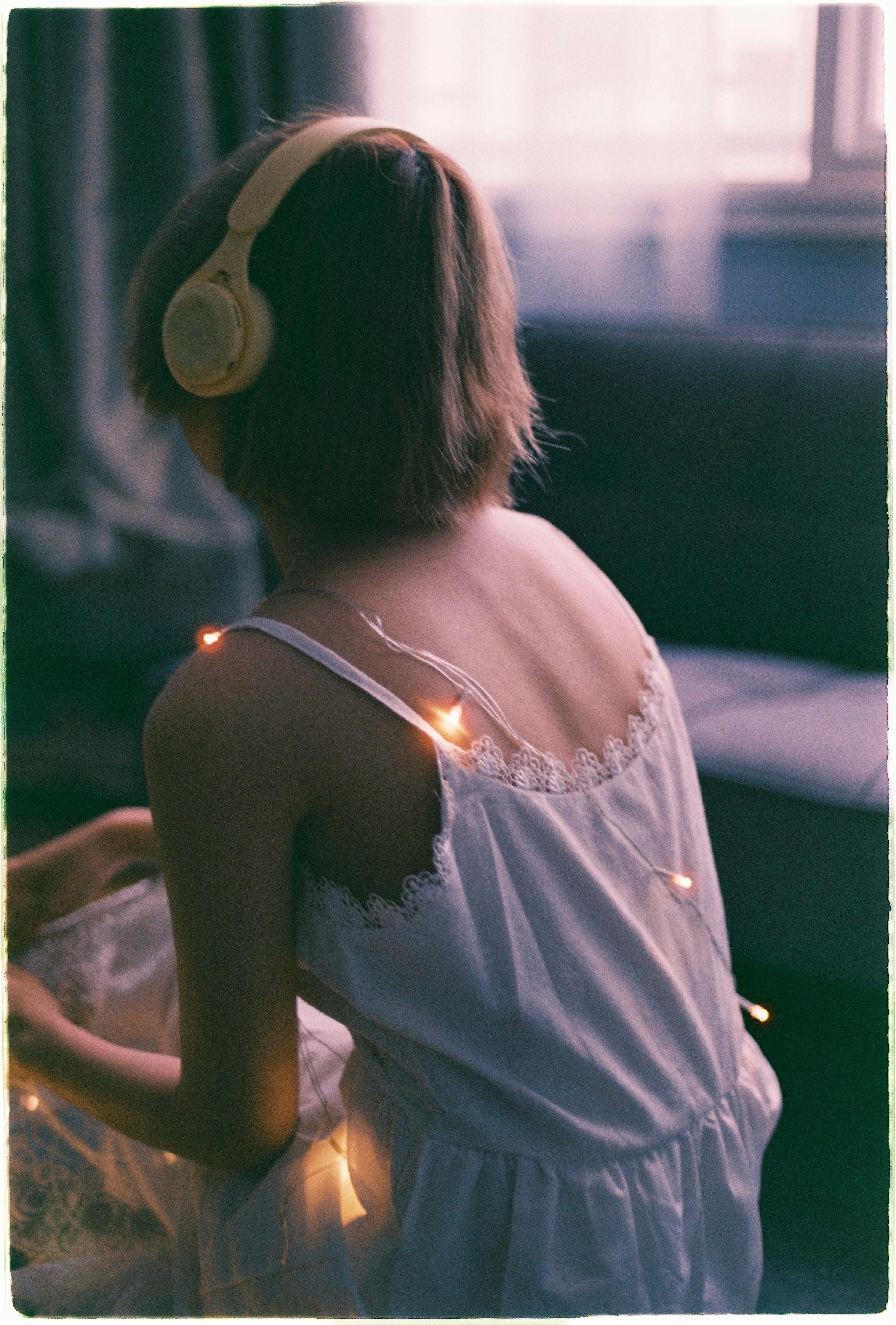 Back view of a woman sitting indoors with headphones and decorative lights on her dress.