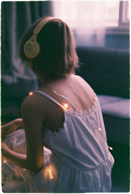 Back view of a woman sitting indoors with headphones and decorative lights on her dress.
