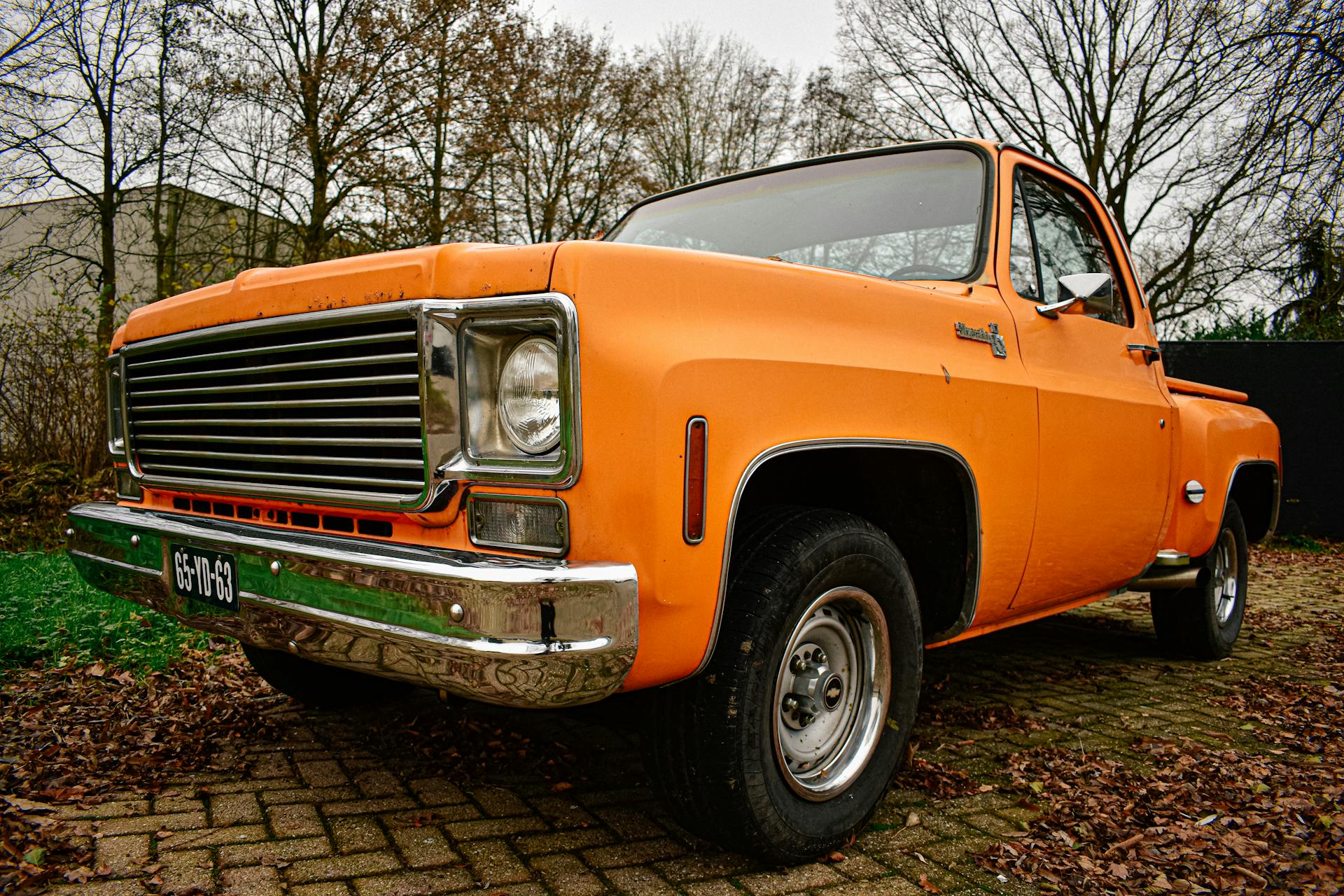 Vintage orange Chevrolet pickup truck parked outdoors with leafless trees.