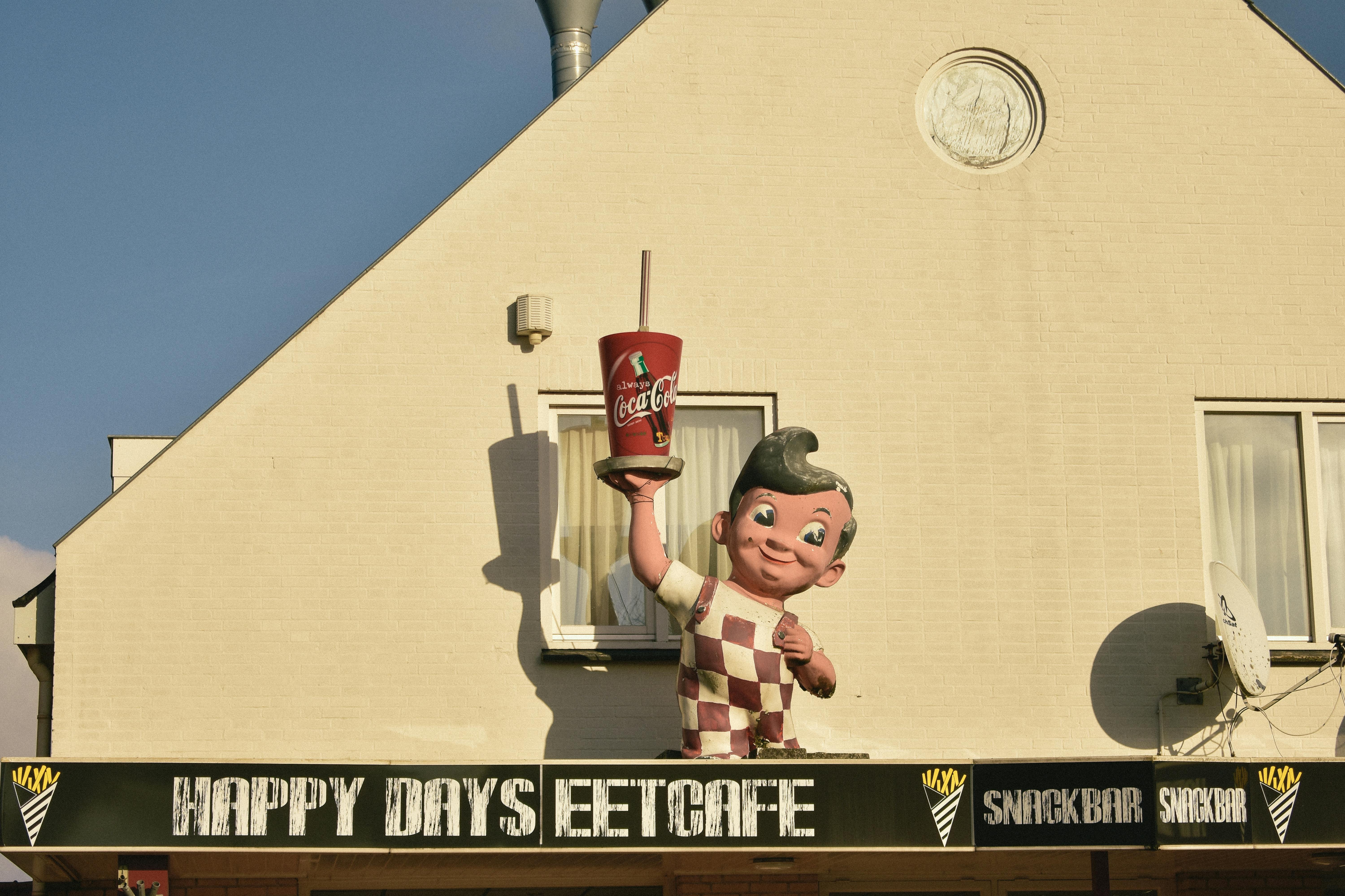 Outdoor signage of a vintage diner featuring a classic mascot statue holding a cola cup.