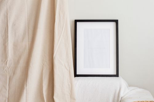 Free A blank black frame rests on a white surface with a beige curtain backdrop, emphasizing minimalism. Stock Photo