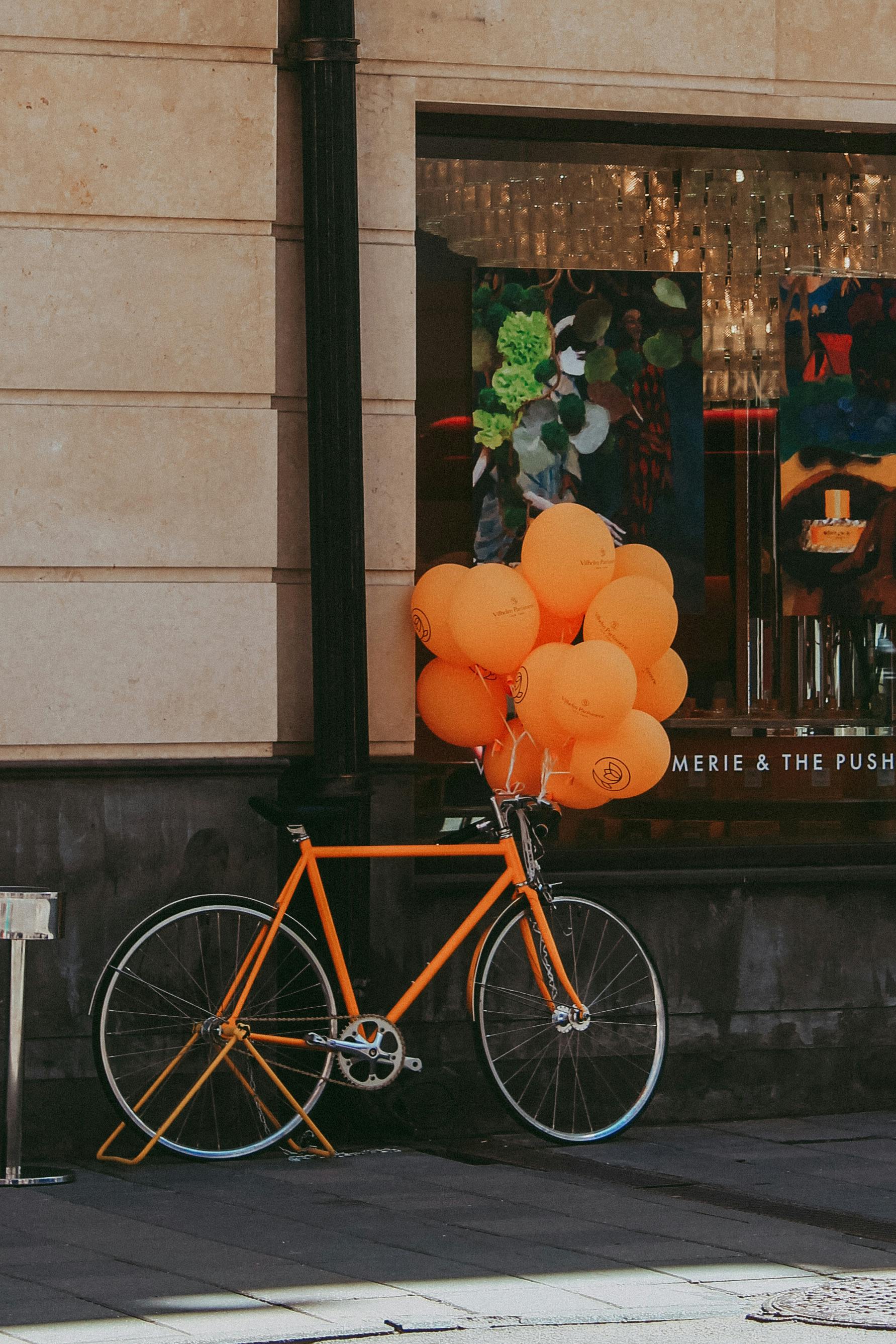 Orange balloons tied to a vintage bike against an art gallery window in the city.