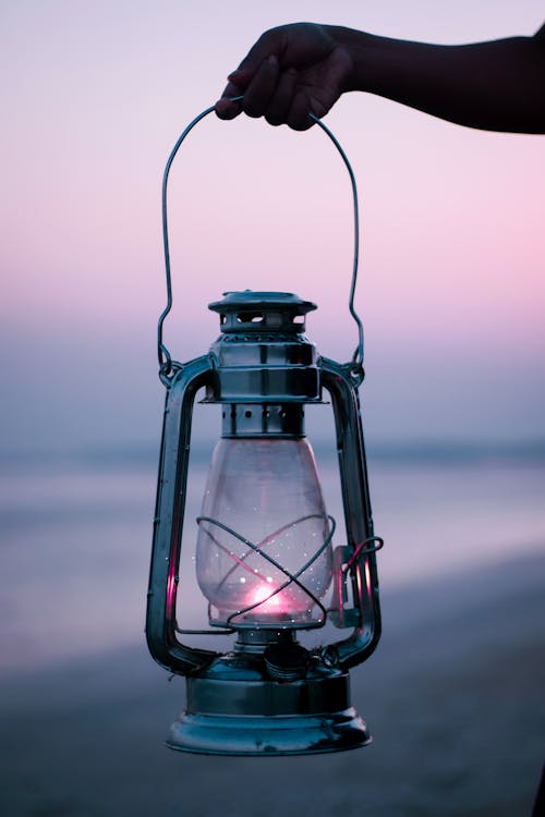 Free Woman Holding a Kerosene Lamp at Dusk on a Beach Stock Photo