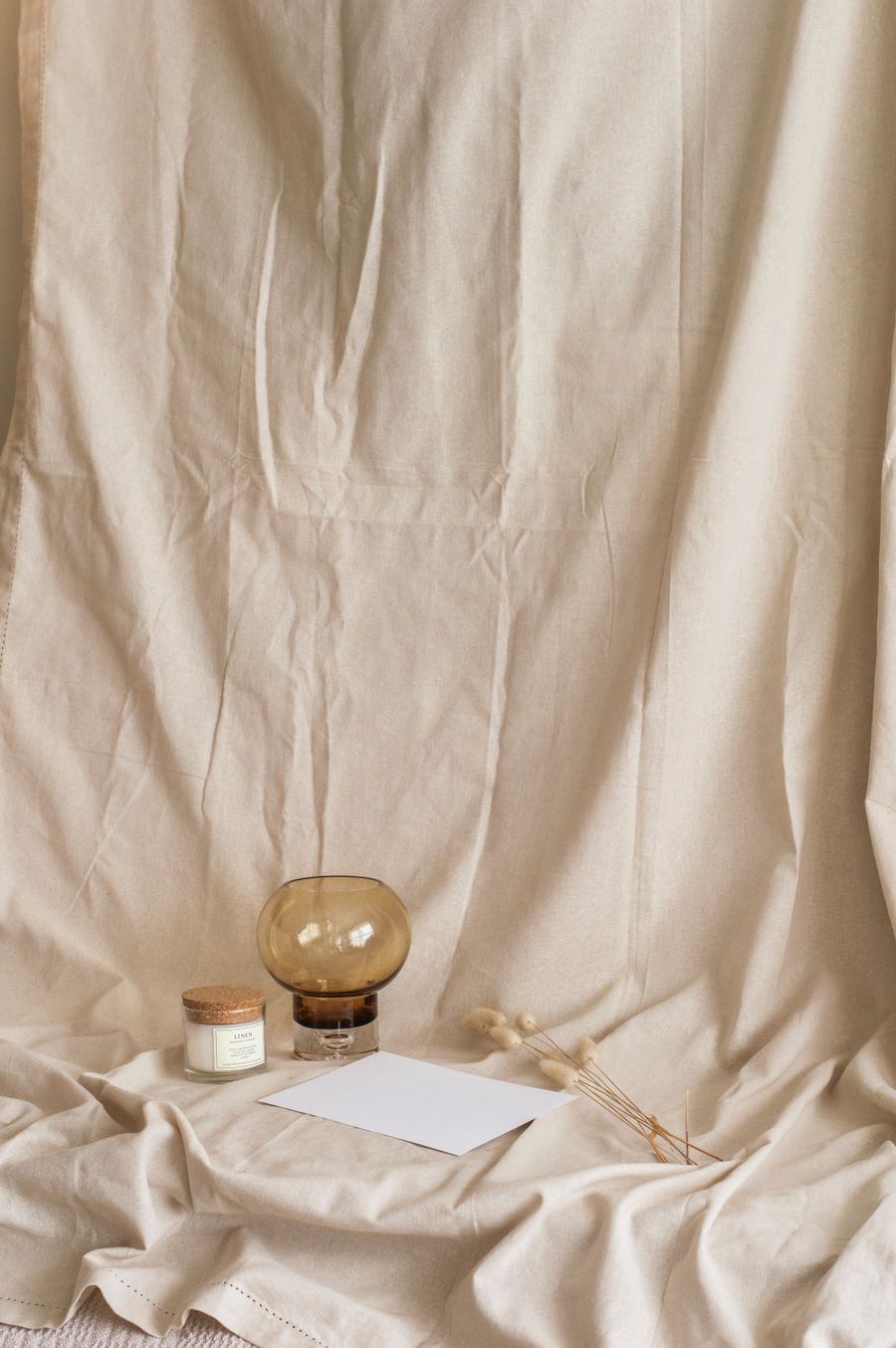 A candle and glass vase on a linen backdrop