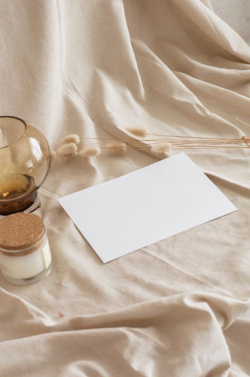 Free Aesthetic still life scene with blank paper, candle, and glass on beige fabric background. Stock Photo