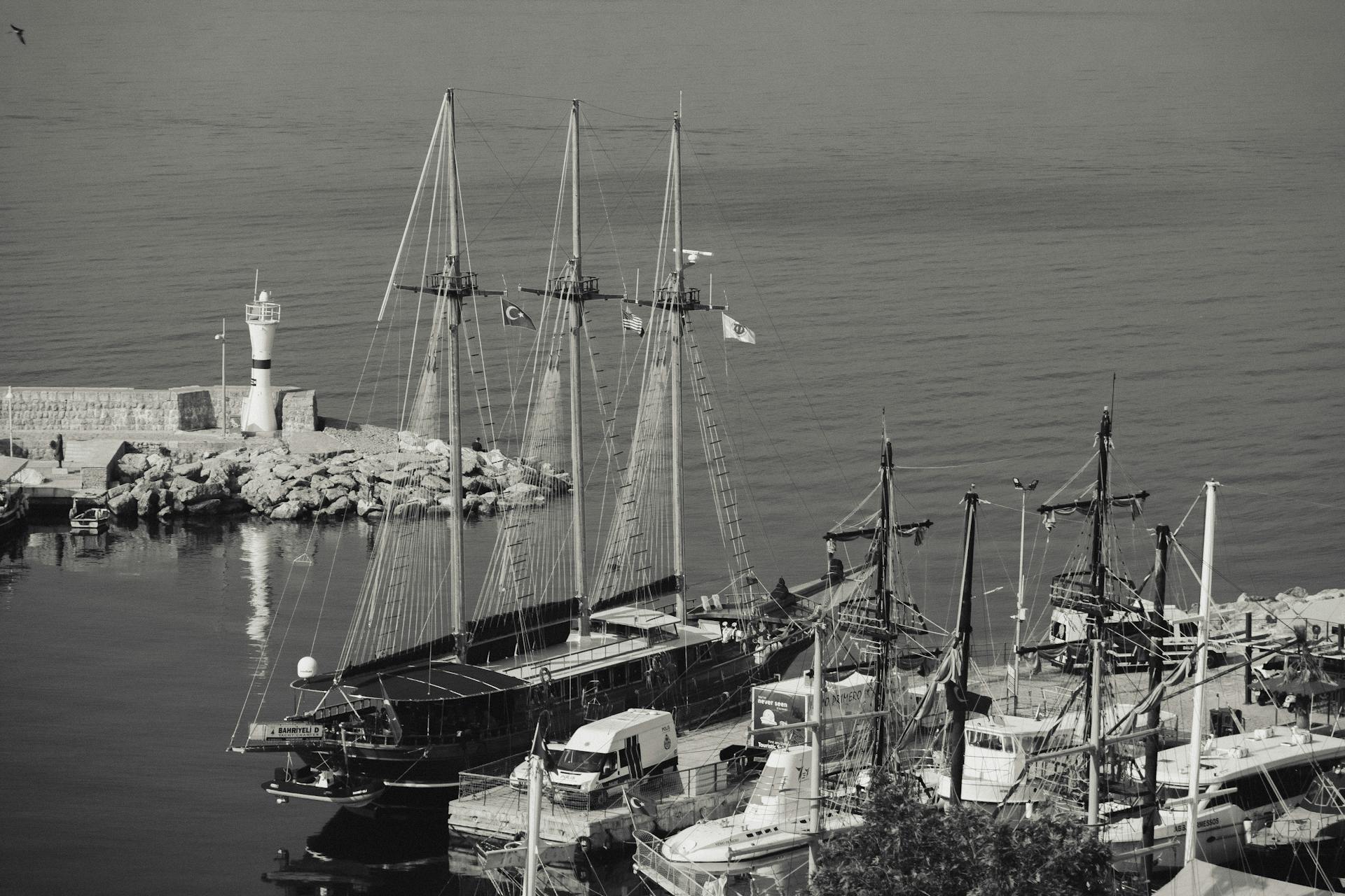 Aerial view showcasing sailboats moored at a bustling harbor with a lighthouse in the background.