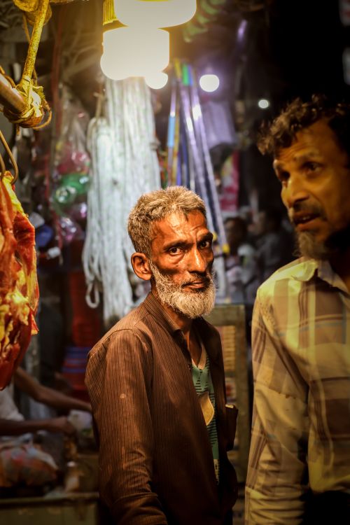 Free An elderly man with a beard stands at a vibrant, traditional market during the night. Stock Photo