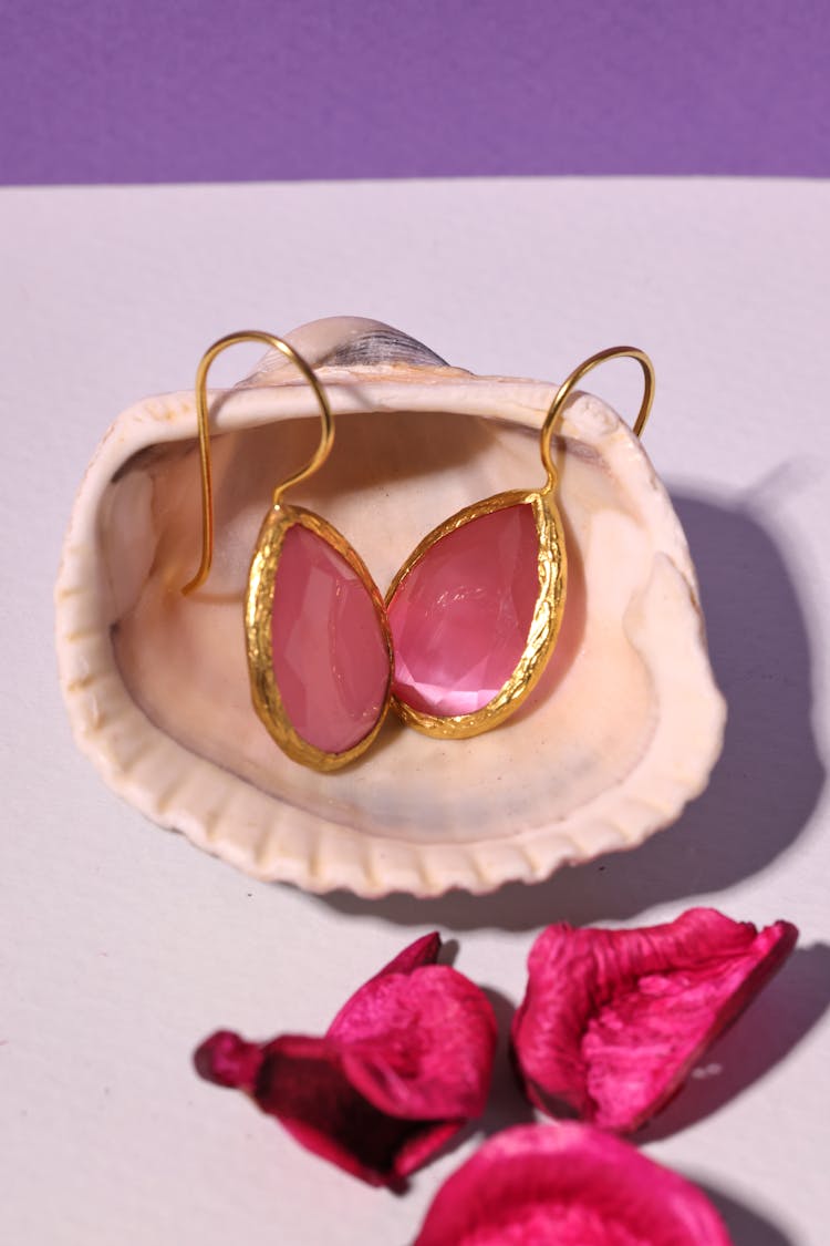 A Pair Of Pink Gemstone Earrings On A Seashell