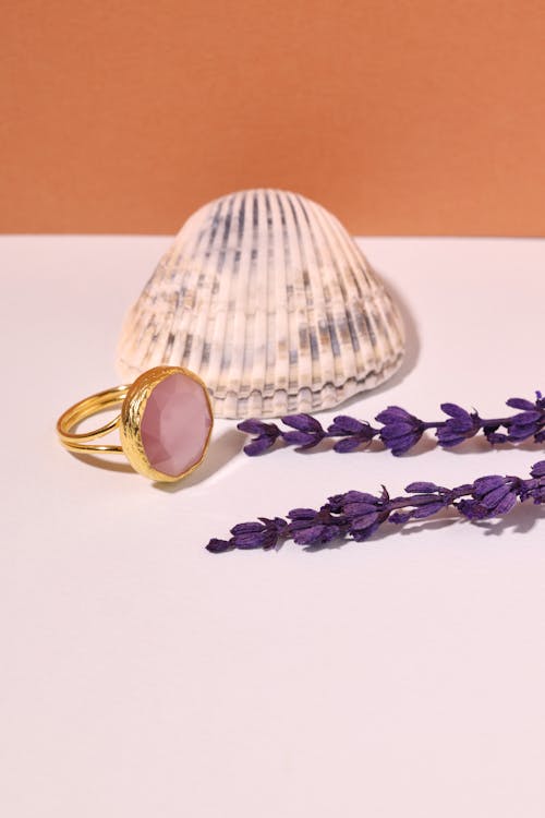 A Pink Gemstone Ring Near Purple Flowers and Seashell
