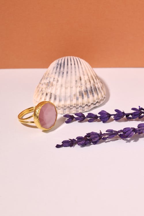 A Pink Gemstone Ring Near Purple Flowers and Seashell

