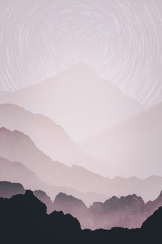 Dreamy mountain silhouette with swirling star trails in a tranquil night sky.