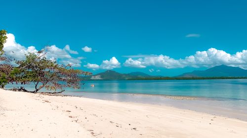 Free Serene view of a tropical beach with azure waters, clear blue skies, and distant mountains, ideal for travel inspiration. Stock Photo