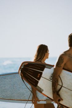 Two young adults with surfboards on a sunny beach, ready for surfing adventure.