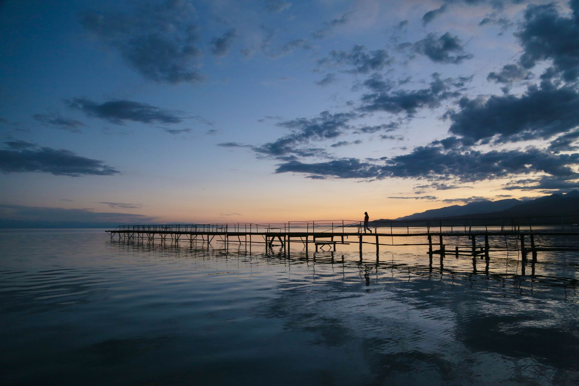 A peaceful pier extends into calm waters during a stunning sunset in Kyrgyzstan, Ak-Talaa District.