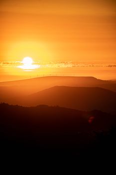 Golden sunset over mountains with silhouettes and scenic backlighting.