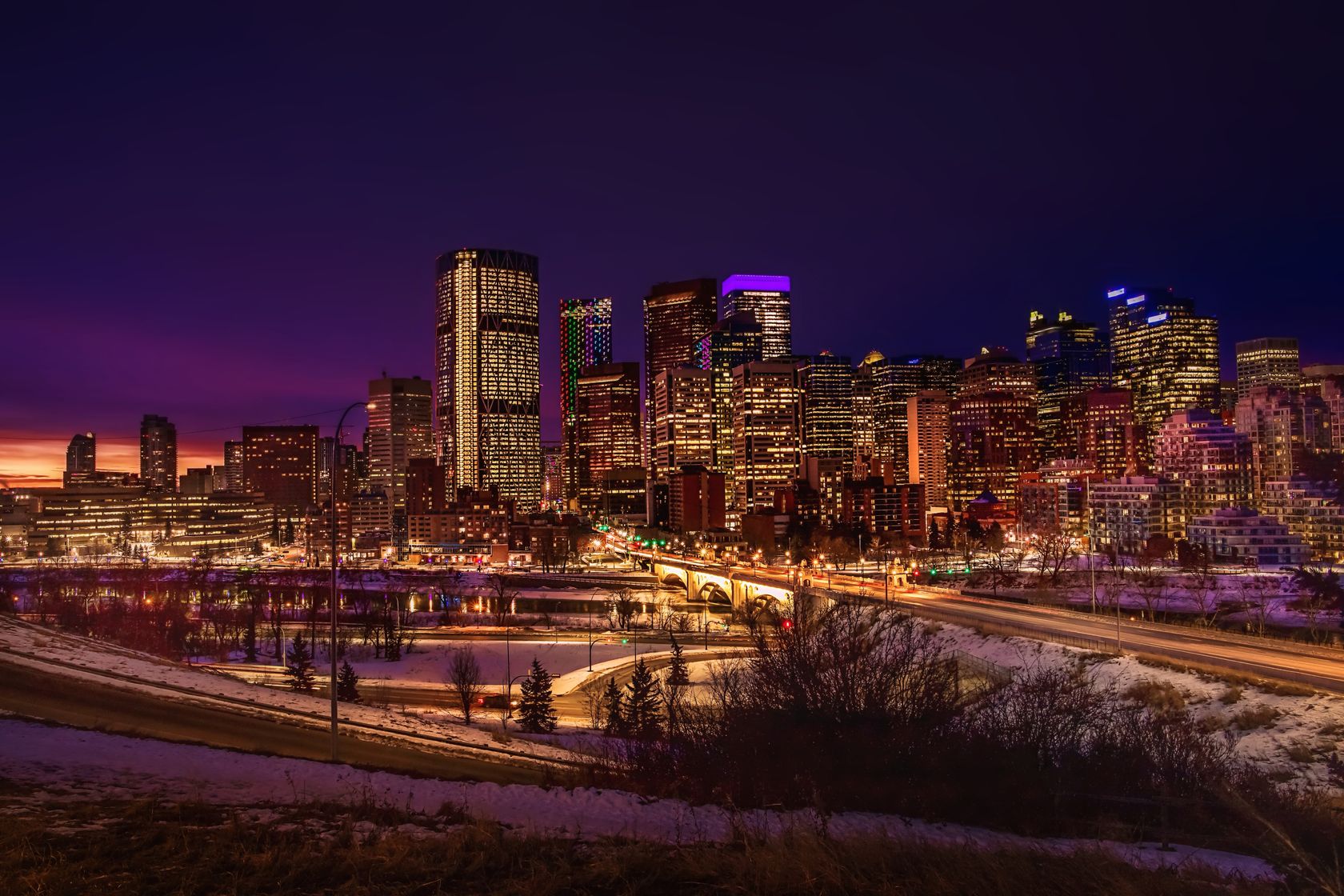 Stunning view of the illuminated Calgary skyline featuring skyscrapers and vibrant city lights at dusk.