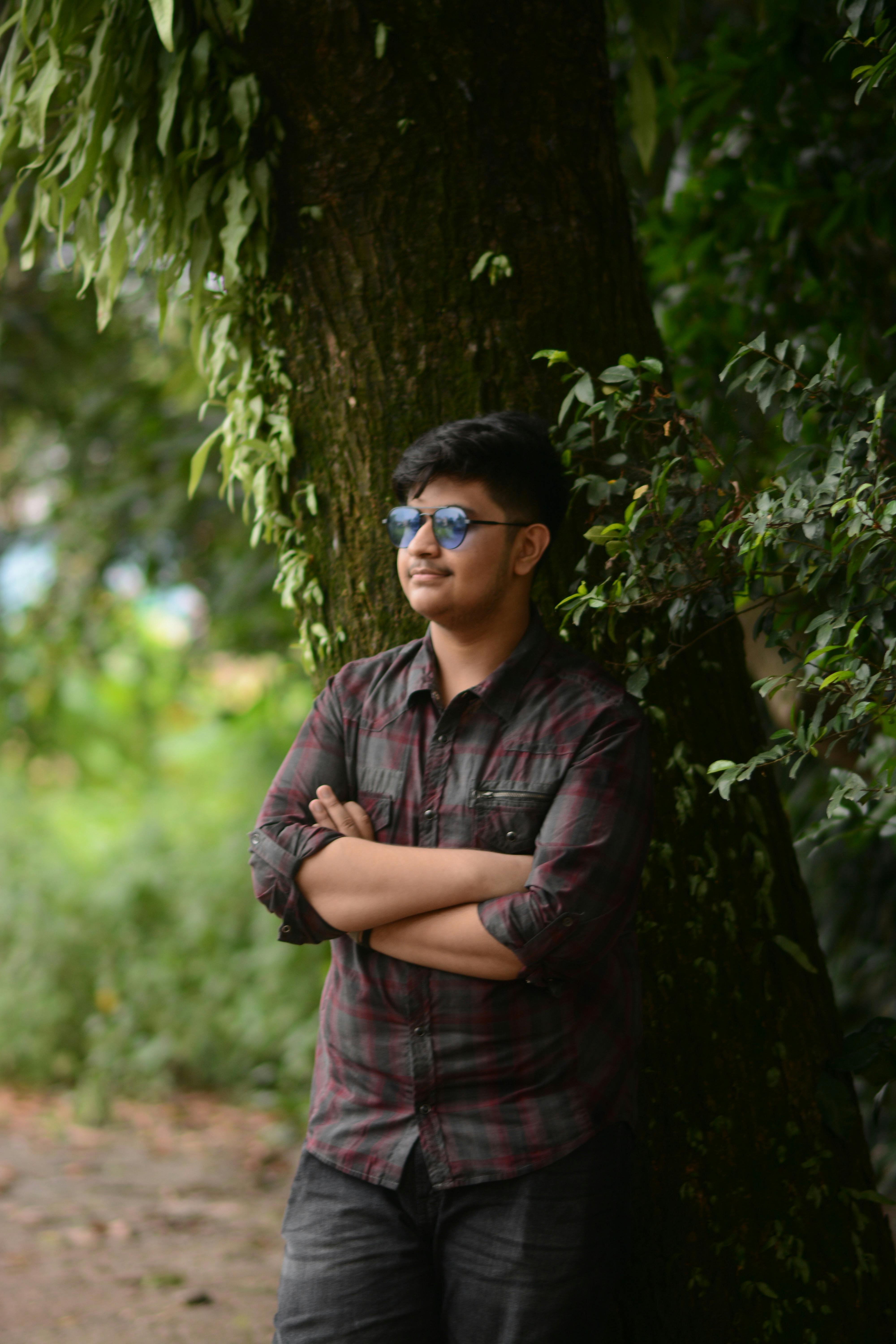 Casual young man with sunglasses leaning against a tree in Brahmanbaria, Bangladesh.