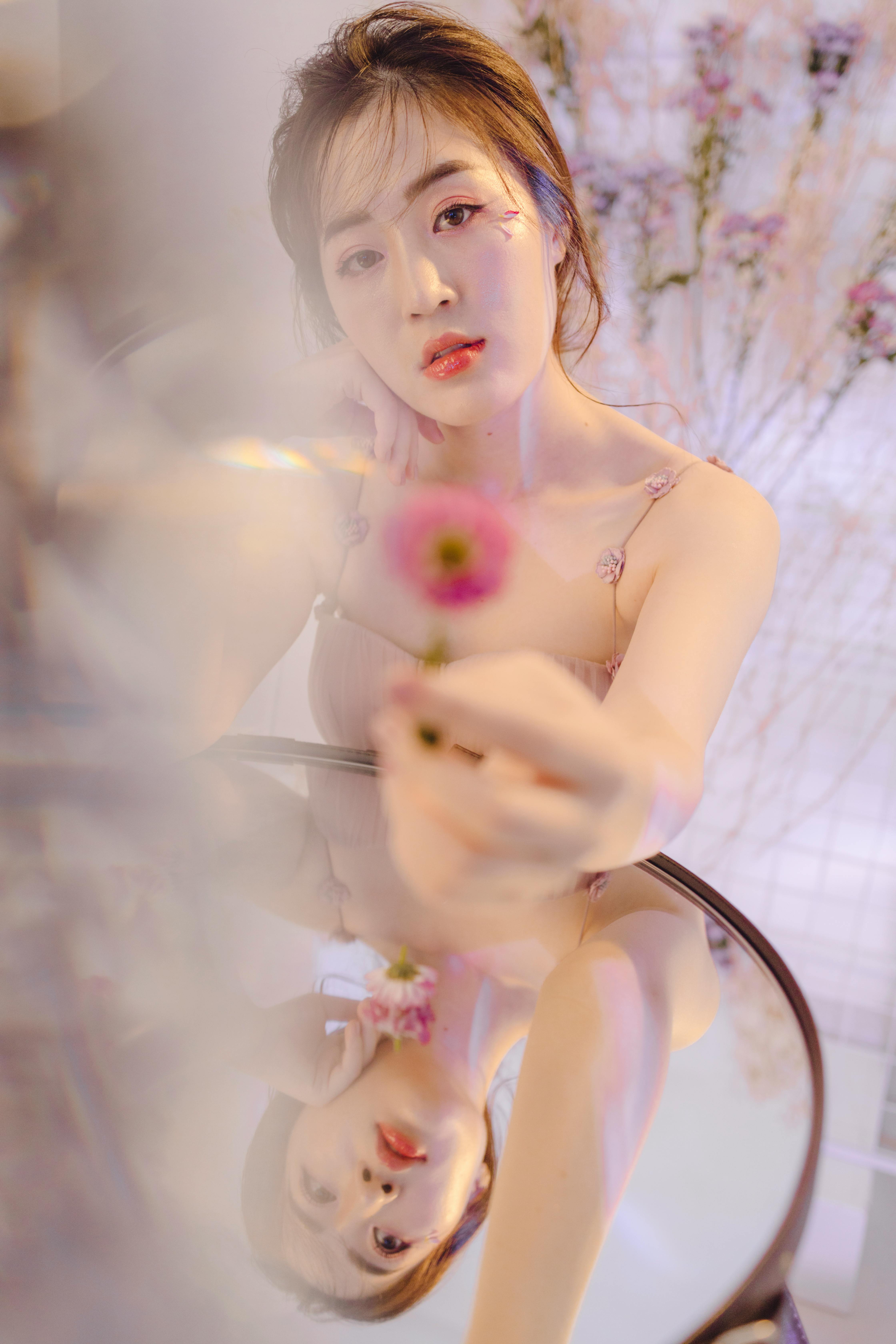 Stunning portrait of a young woman holding a pink flower with a reflective surface.