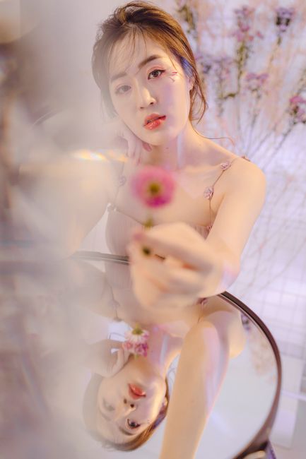 Stunning portrait of a young woman holding a pink flower with a reflective surface.