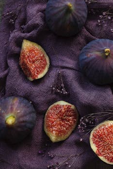 Aesthetic flat lay of fresh figs on a textured purple fabric background.