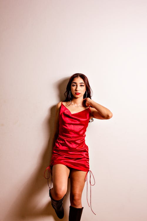 A Woman in Red Spaghetti Strap Dress leaning on Wall