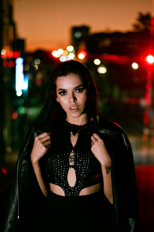 Free Elegant woman wearing a black leather jacket posing on a vibrant city street at night. Stock Photo
