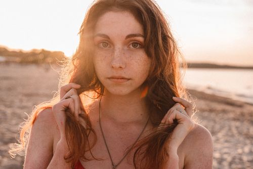 Free A teenage girl gazes calmly at the camera, bathed in warm sunset light on a beach. Stock Photo