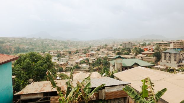 Aerial view of Yaoundé, Cameroon showcasing rooftops and lush greenery under a foggy sky.