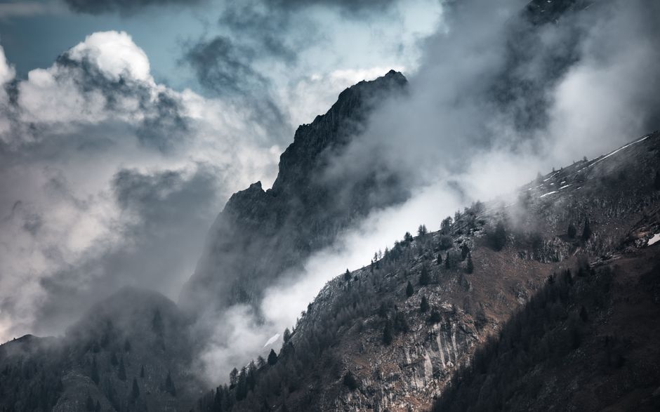 Dramatic view of rocky mountain peaks shrouded in mist and clouds, capturing nature's majestic beauty.