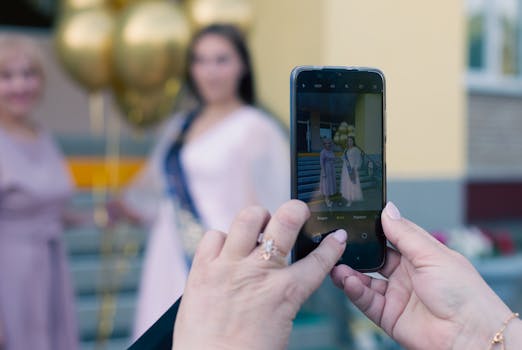 Close-up of hands holding a smartphone taking a photo of two women with balloons.