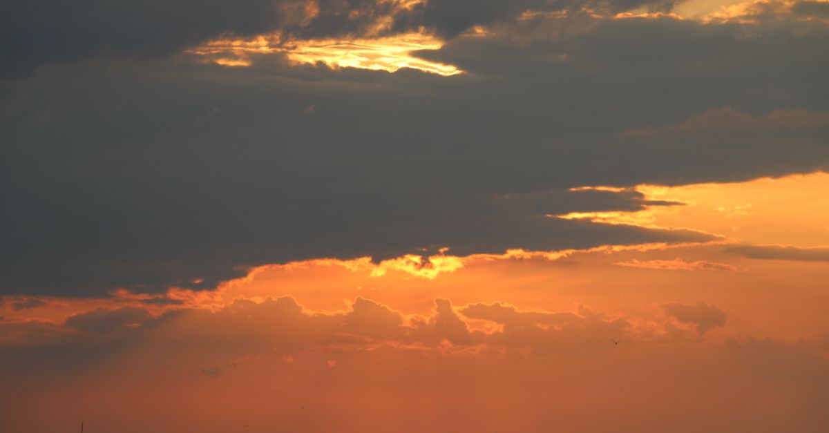 Dramatic clouds and golden sunset create a stunning view over an ocean beach.