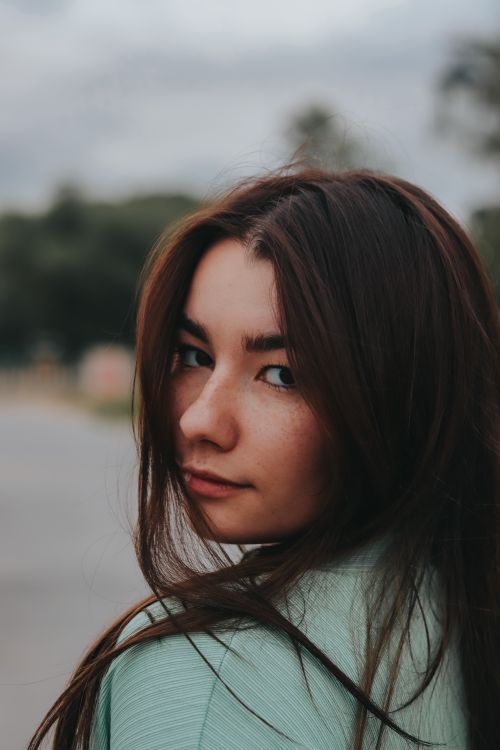 Free Portrait of a young brunette woman outdoors, looking over her shoulder with soft focus background. Stock Photo