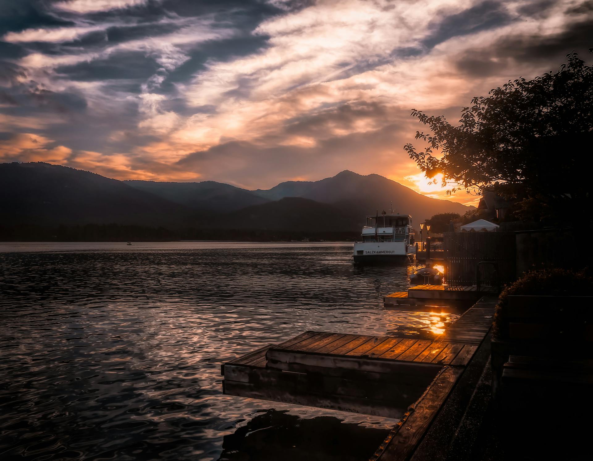Beautiful sunset view of a boat docked on a calm lake with mountains and a vibrant sky.