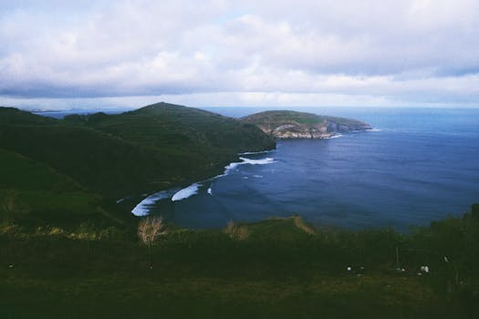 Breathtaking view of Azores' coastline with lush hills and blue ocean waters under a cloudy sky.