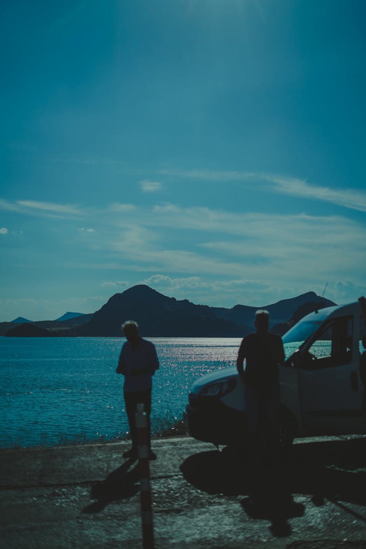 People Silhouettes Next To A Parked Car