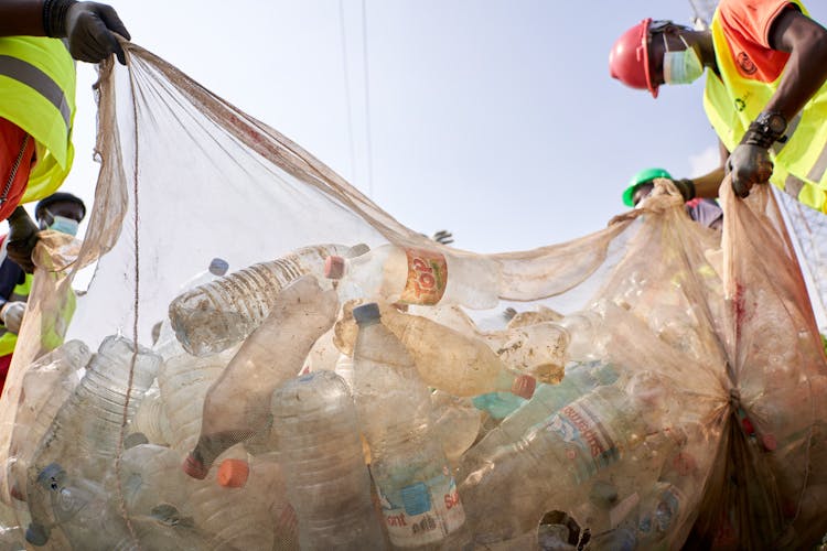 Low Angle Shot Of People Holding A Garbage Bag Full Of Plastic Bottles