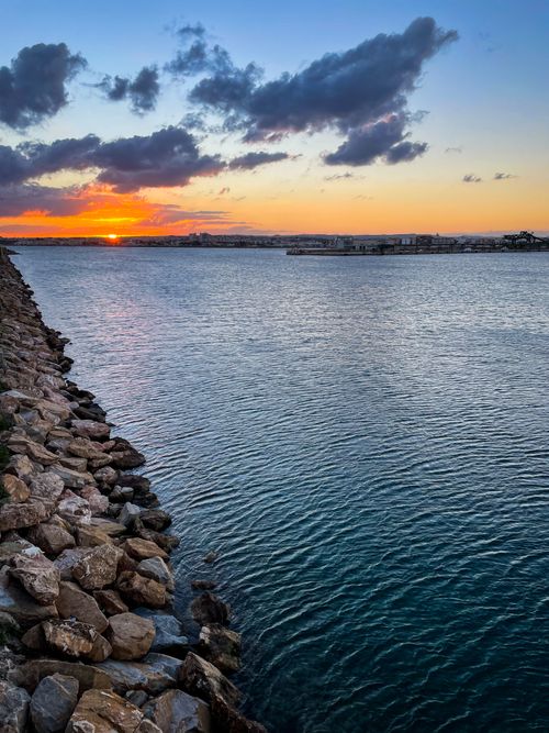 Free Beautiful coastal sunset over calm waters with a rocky shoreline. Stock Photo