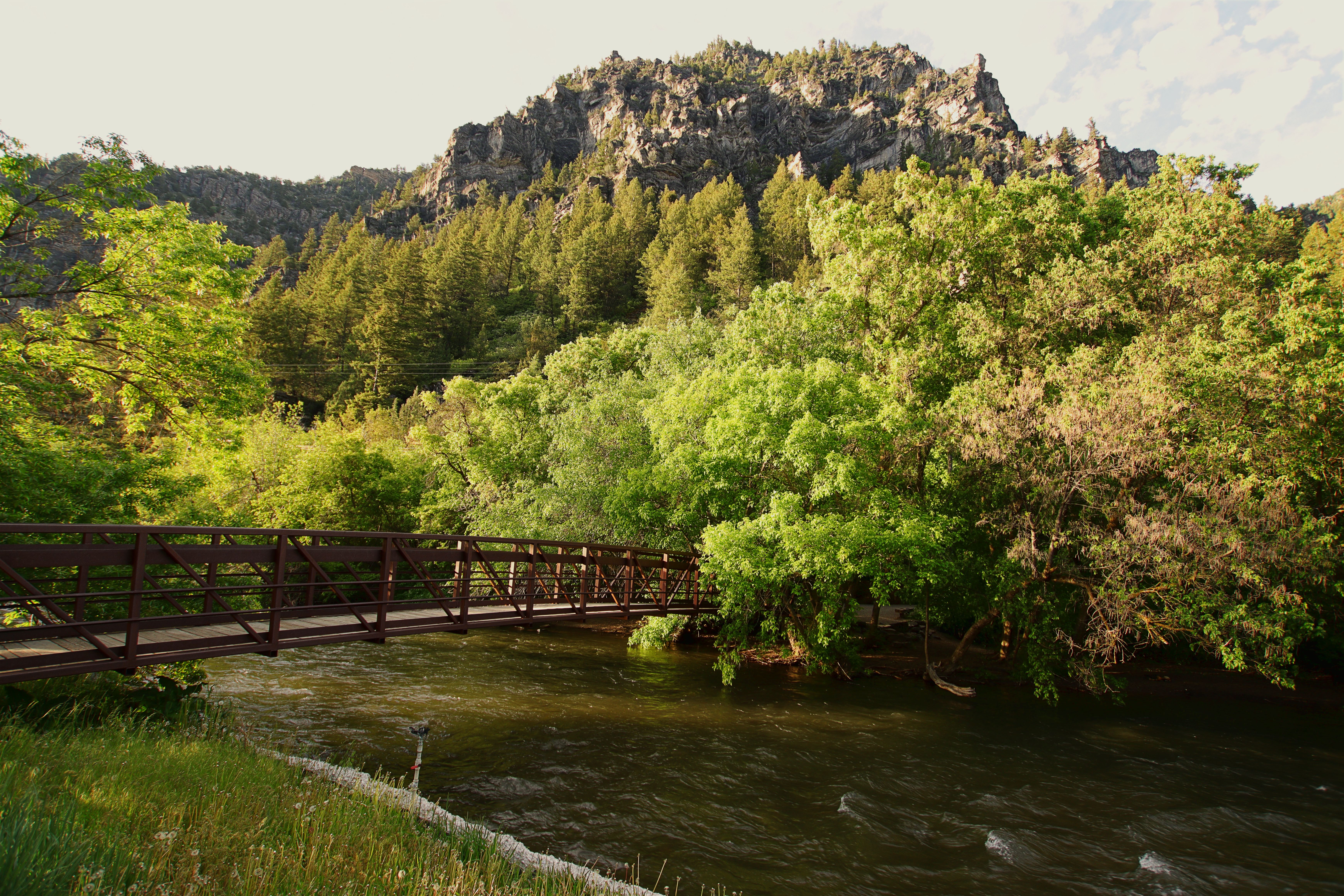 A picturesque bridge over a flowing river, surrounded by lush trees and a mountain backdrop.
